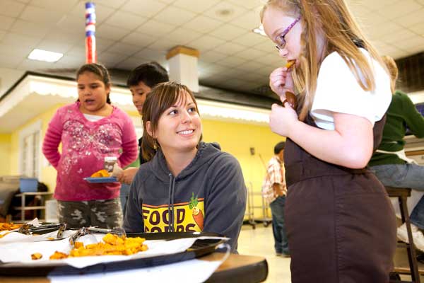 A FoodCorps servicemember watches as an elementary student tries squash fries in Traverse City, MI.