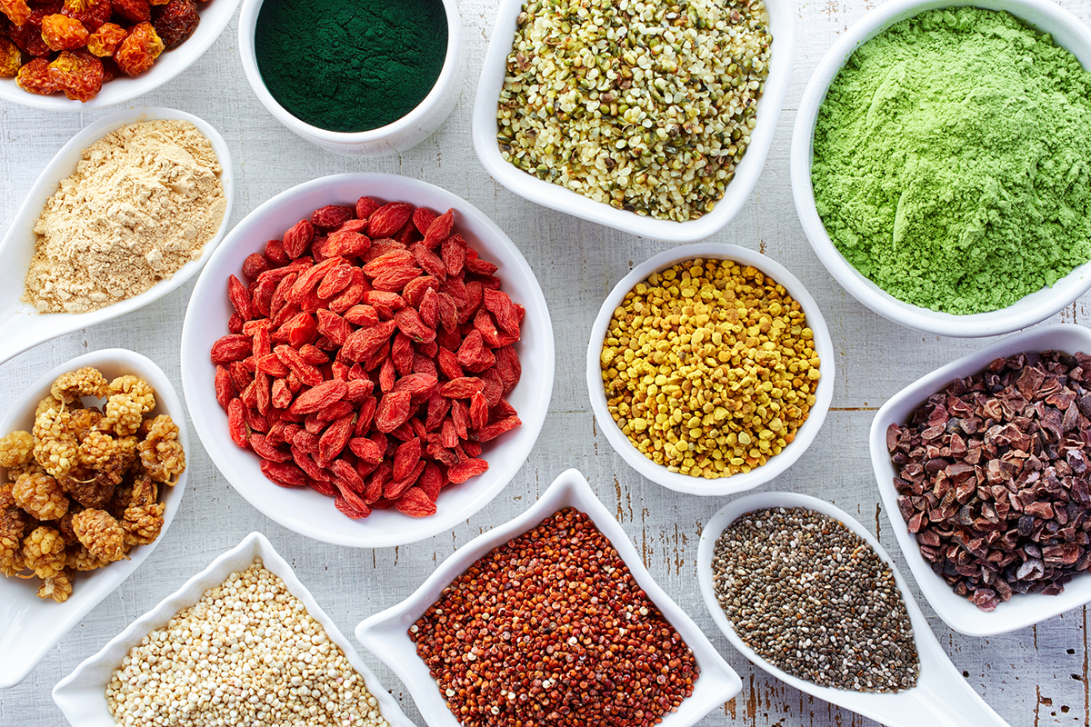 White bowls of various superfoods on white wooden background