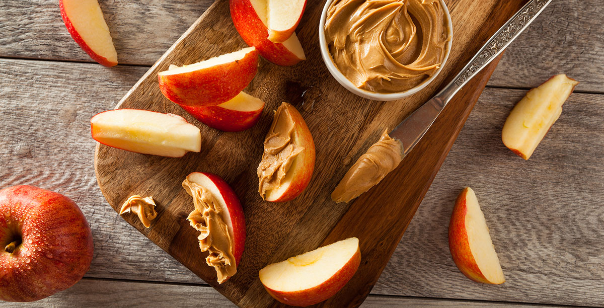 cut-up apples with a jar of peanutbutter and a knife 
