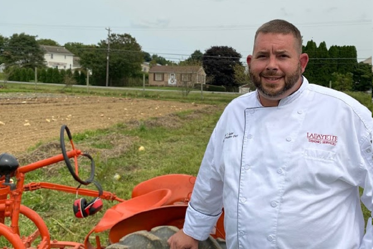 Chef stands next to an orange tractor in a field