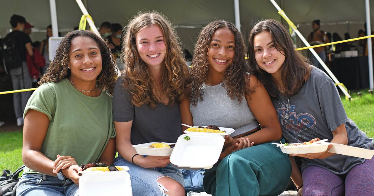 Smiling students pose with to-go containers full of local clams, corn, and other sides.