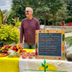 A smiling farmer standing behind a table with vegetables on it