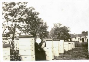 An old photograph of a nun posing next to a large apiary