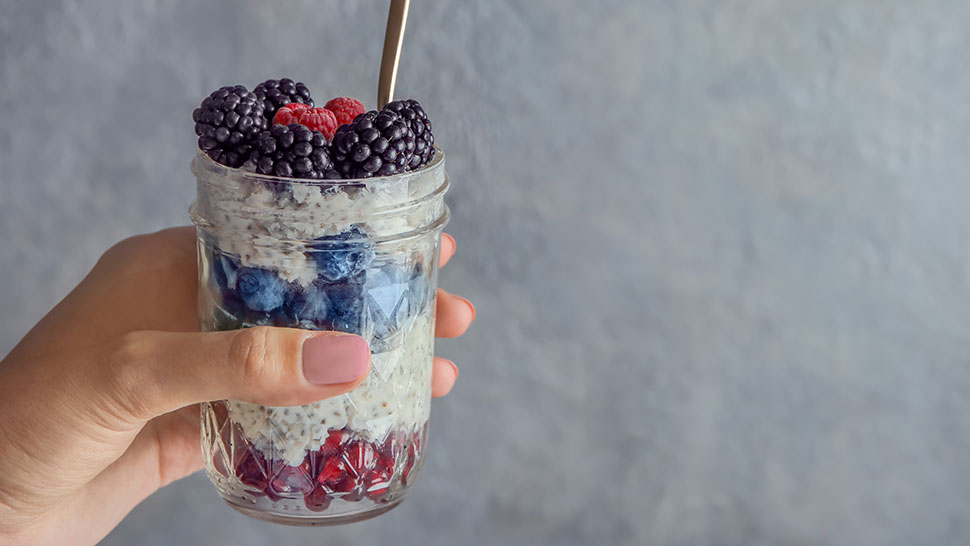 A hand holding a chia and berry parfait with a grey background