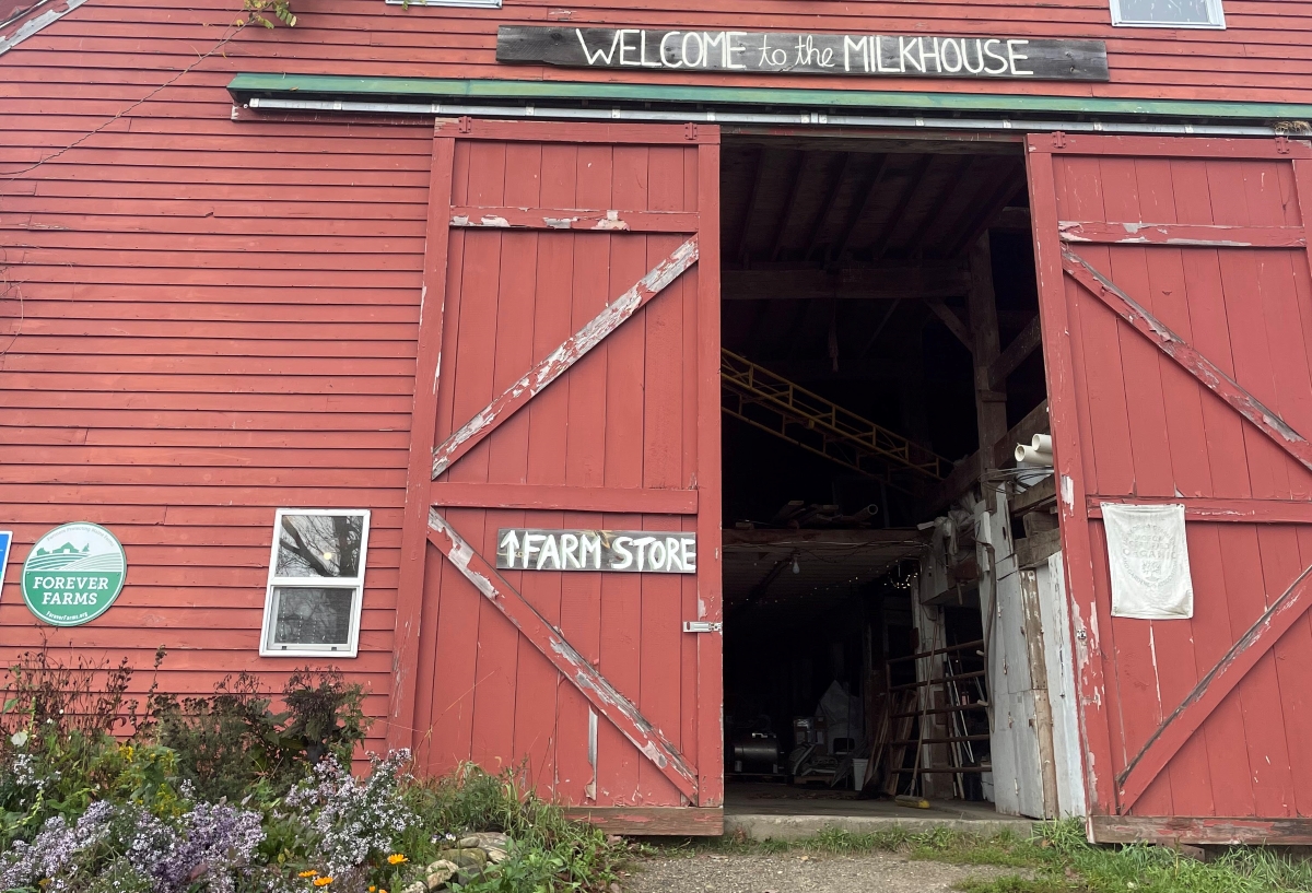A large barn door, half open with a sign that reads "welcome to the Milkhouse"