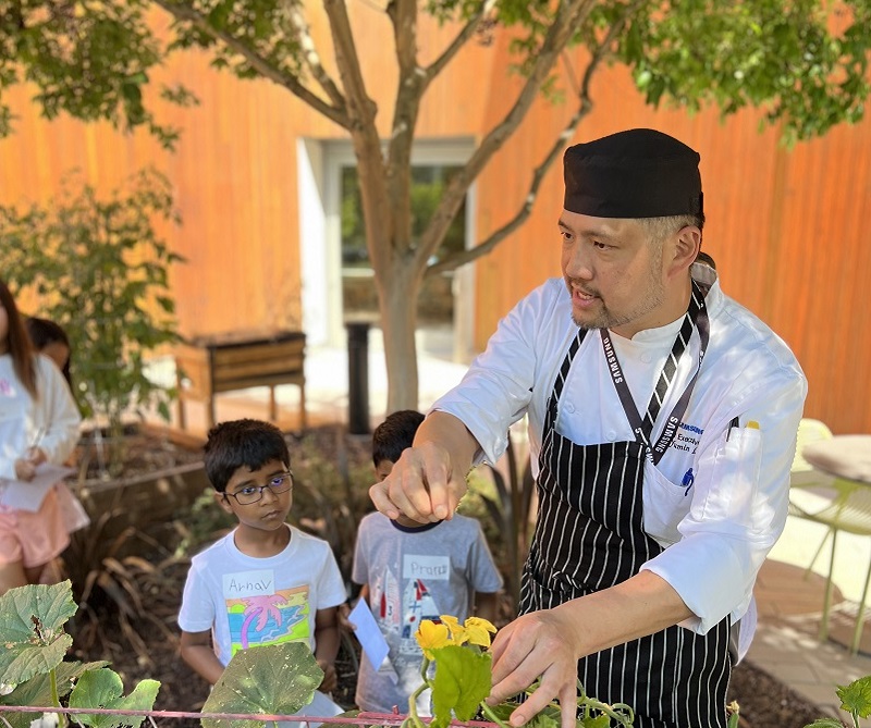 A Bon Appetit chef shows kids vegetables growing in his cafe's garden. 