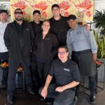 A group of co-workers poses in front of an image of wheelbarrows filled with produce.