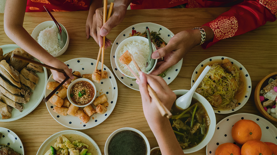 An overhead shot of a feast table with people's hands reaching for food. 