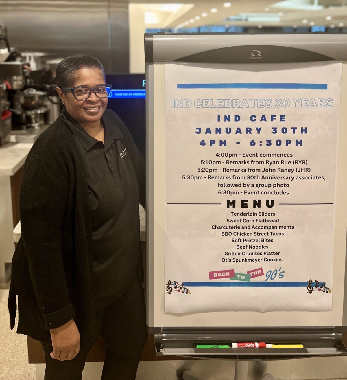 A woman stands next to a large sign featuring a menu for an event.