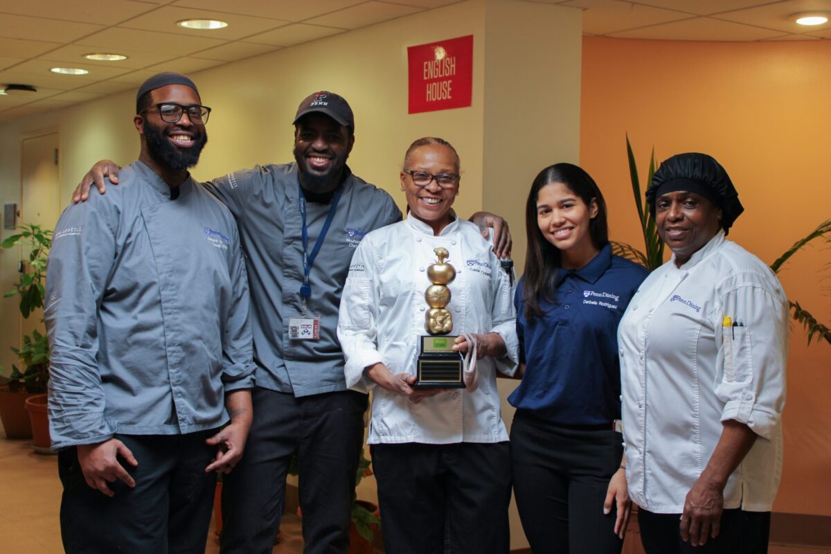 A group of five culinary professionals stand together holding a trophy