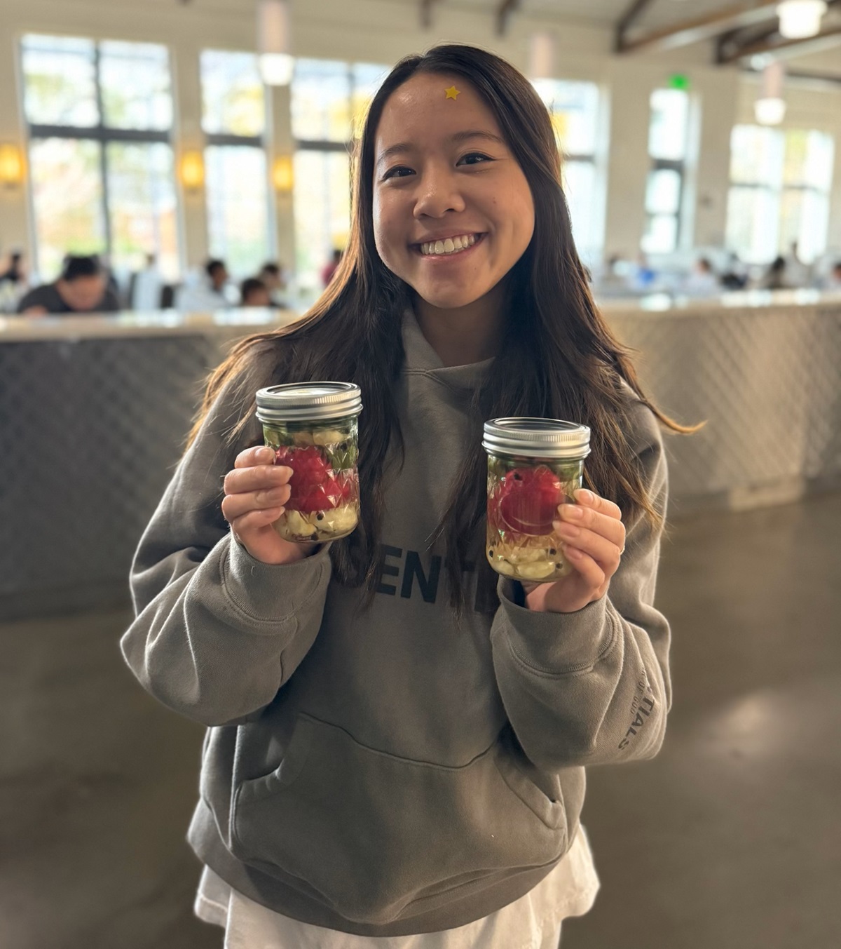 A smiling young woman with long brown hair holds up two jars of pickles