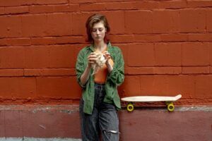 a young woman has a snack in front of a wall with a skateboard behind her