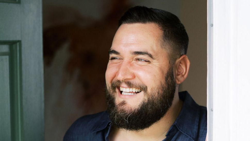 A headshot of a smiling man with a beard and a nose ring. 