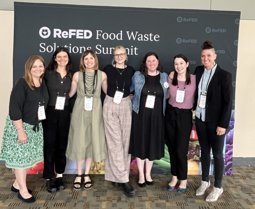A group of people stand in front of a sign for a food waste conference.