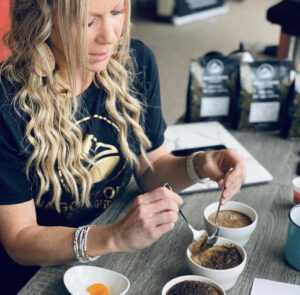 A woman with long wavy blonde hair sets up for a coffee cupping.