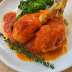 A closeup photos of braised chicken with greens and mashed potatoes.