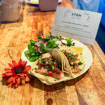 A plate of fish tacos with a salad, garnished with an orange flower on a wooden countertop.