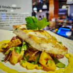 A piece of seared fish over eggplant panzanella. Signage in background.