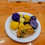 An overhead shot of steamed yellow and purple cauliflower with a piece of roasted chicken.