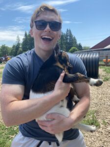 A young man holds a baby goat at a farm.