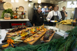 Cooks in a university setting stand behind platters of food.