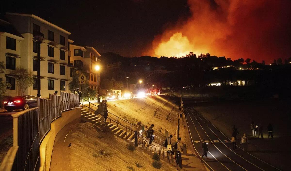 People evacuate a college campus as a fire burns behind them.