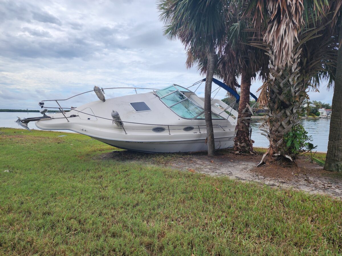 A post-hurricane scene where a white boat has run aground onto a lawn