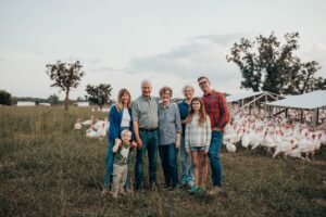 A family of farmers standing in a field with their turkey flock behind them.