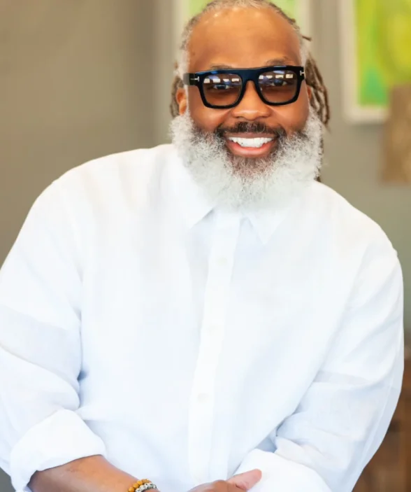 A man in a white shirt with a big white beard and glasses, smiles at the camera