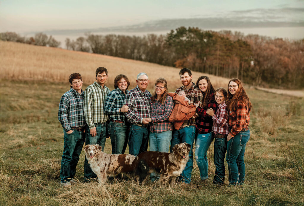 A large family all wearing plaid flannel shirts poses for a portrait in a farm field.