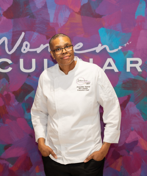 A woman chef in her white chef's coat stands in front of a blue and purple background with the words Women in Culinary behind her.