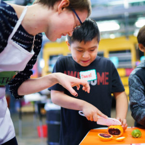 Young woman helping boy use a knife