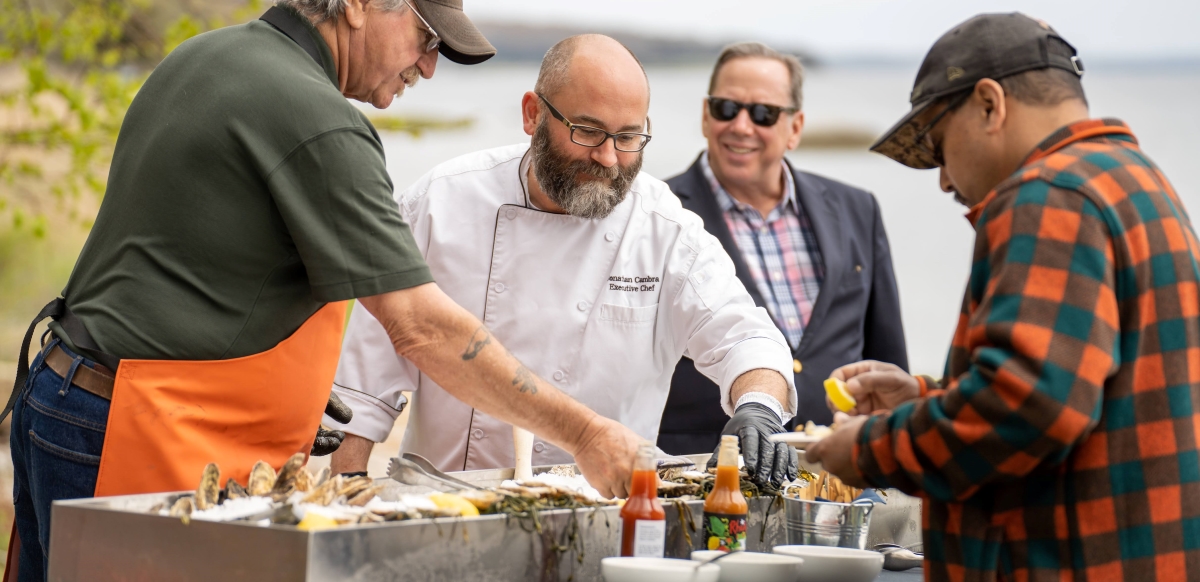 A group of people including a chef gather around a raw bar