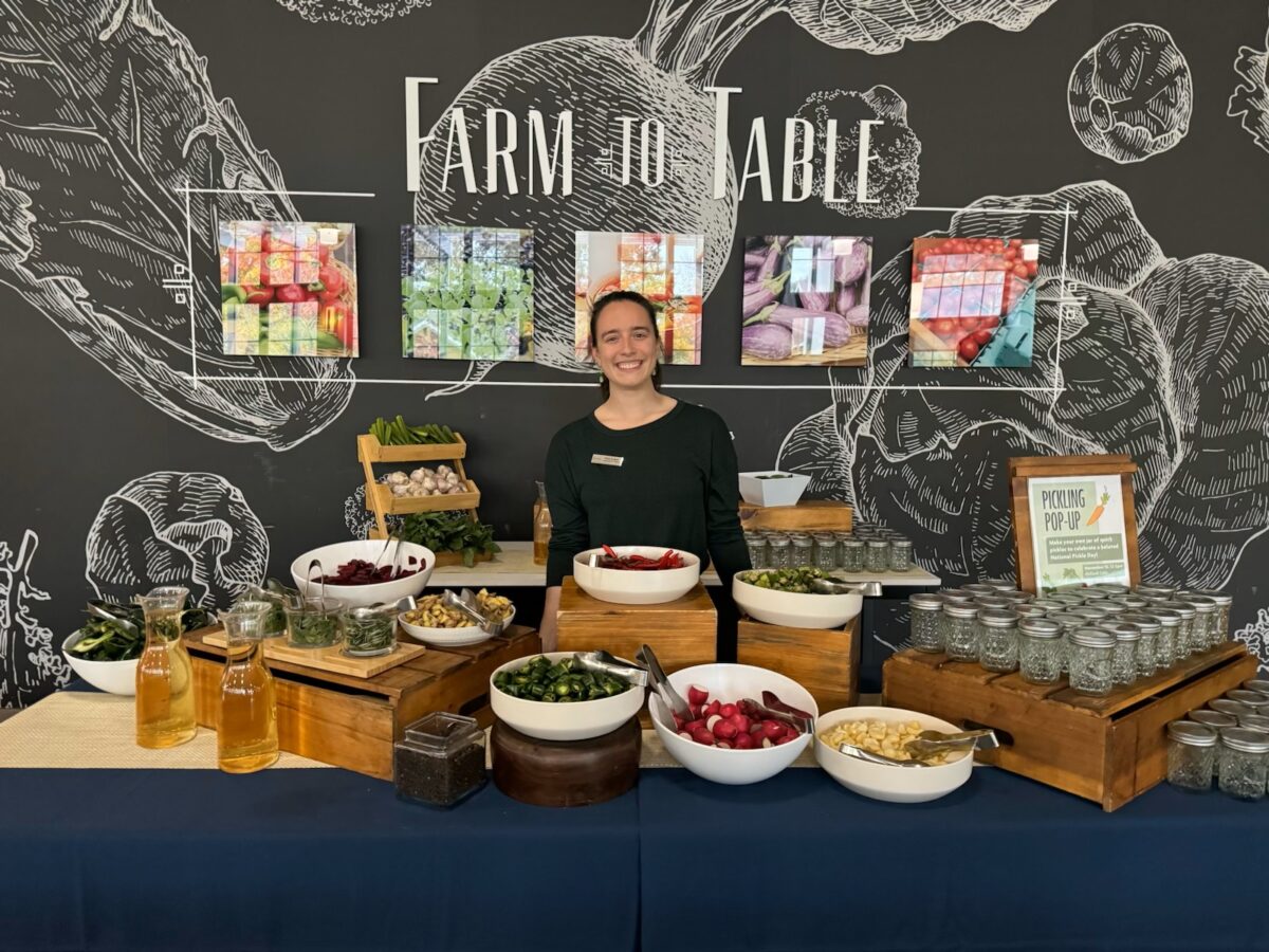 A young woman stands behind a farm to table display with bowls of produce arrayed in front of her.