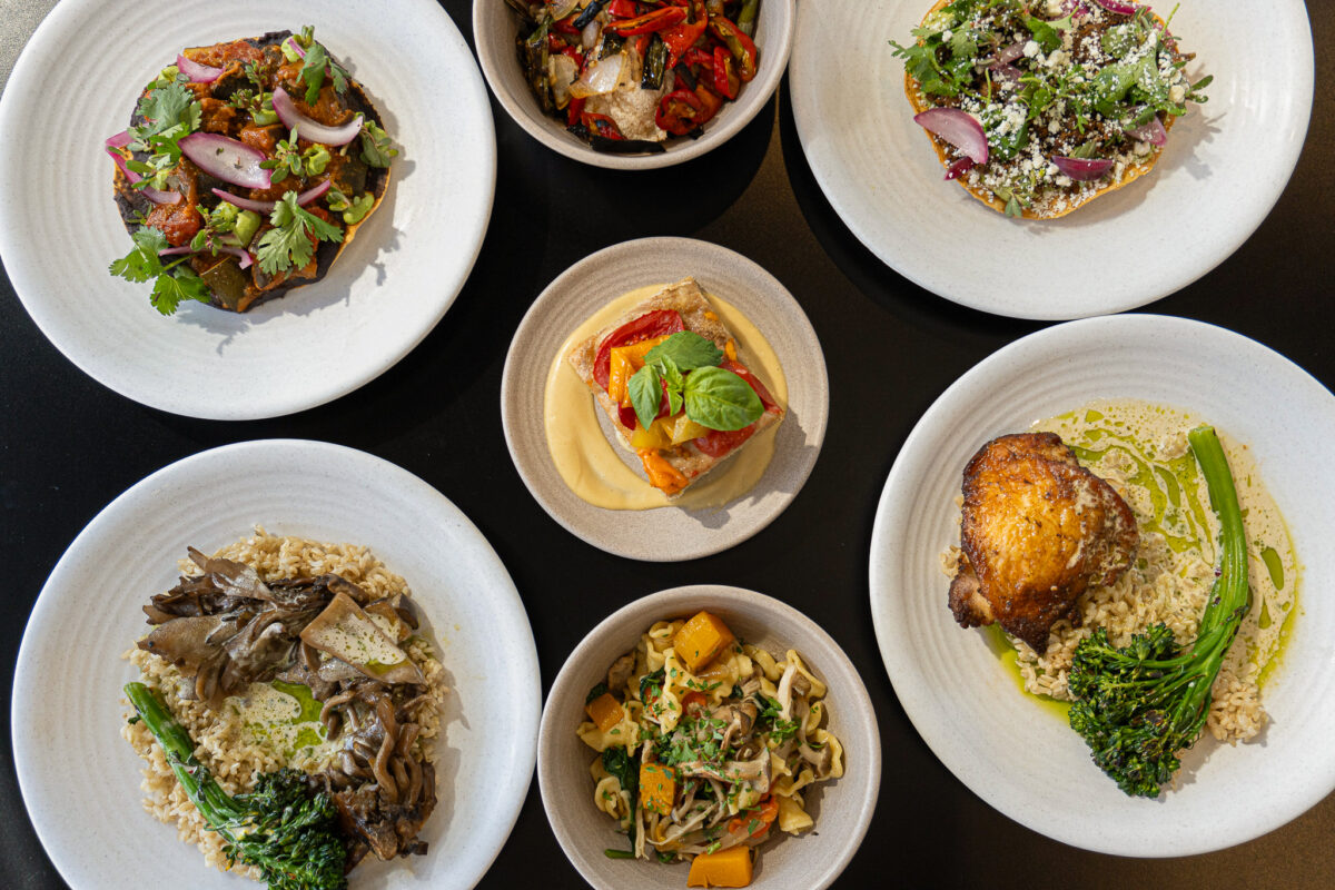 An overhead shot of seven dishes of high-end, artfully plate food on white plates. 