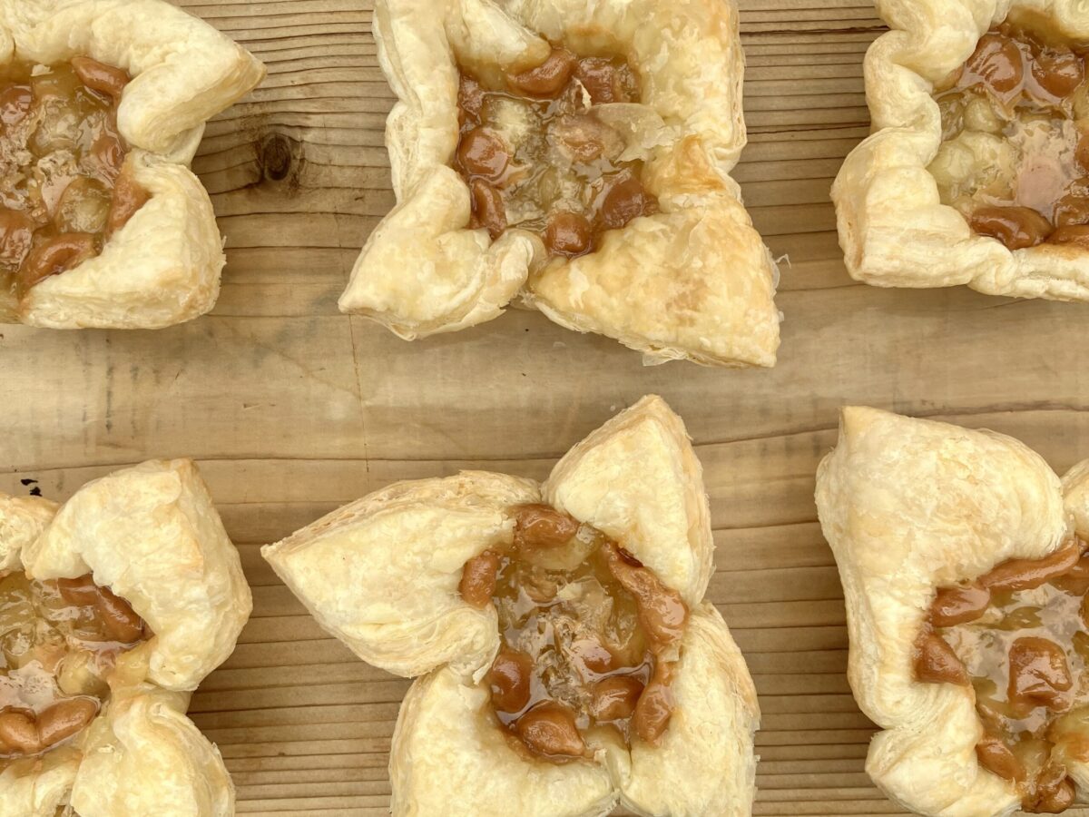Rows of puff pastry tarts with apple filling on a wooden board.